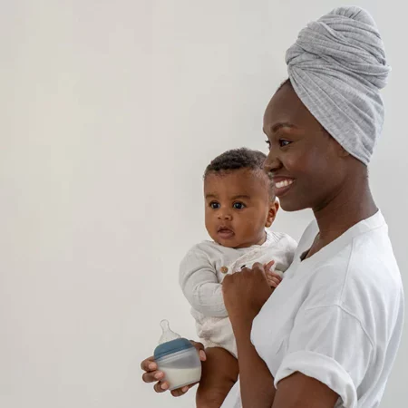 une maman portant son bebe en tenant dans une main un biberon élhée
